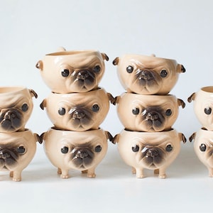 May include: A collection of ceramic pug-shaped planters. The planters are beige with dark brown accents on the face and ears, and black eyes. Each planter has a small handle on each side and four small feet. The planters are stacked in rows.