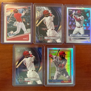 Peut inclure: Cinq cartes de baseball à collectionner représentant un joueur de baseball en uniforme rouge et blanc. Les cartes sont dans des pochettes en plastique de protection. Les cartes présentent le nom du joueur "JD ADELL" et le logo de l'équipe.