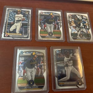May include: Five baseball trading cards featuring a baseball player in a Milwaukee Brewers uniform. The cards are silver and have a holographic finish. The player's name, "Jackson Chourio", is printed on each card.