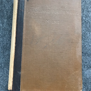 Puede incluir: Un libro antiguo titulado "Standard Arithmetic" de Milne. La portada es de color marrón descolorido con texto en relieve. El lomo es negro con un borde color crema. Es una "Edition Without Answers".