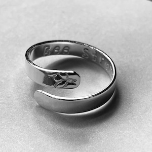 May include: A silver ring with the words "Bee Strong" engraved on the band.