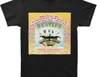 Op de afbeelding: Zwart T-shirt met een afbeelding van The Beatles' "Magical Mystery Tour". Het ontwerp bevat de bandnaam, de tourtitel en andere tekst op een gele en oranje achtergrond. Het shirt heeft een ronde hals.