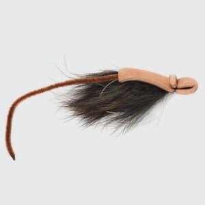 May include: A fishing fly lure featuring a tan leather-like body with a looped end, accented by a dense tuft of dark brown animal hair and a long, thin, flexible brown chenille tail extending from the base of the textured hair section.
