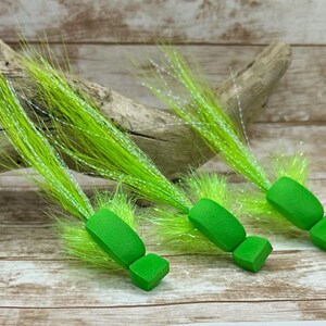 May include: Three lime green fly fishing lures with long, bright green and white fibres. The lures are made of foam and have a rectangular shape.