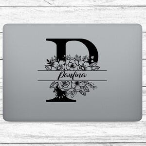 Könnte beinhalten: Ein schwarzes Blumenmonogramm mit dem Buchstaben "P" und dem Namen "Paulina" in Schreibschrift. Das Design befindet sich auf einem grauen Laptop mit weißem Holzgrund.