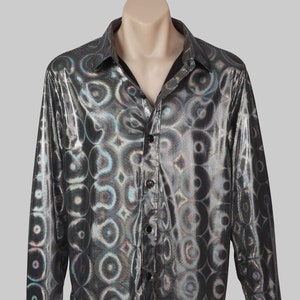Op de afbeelding: Een zilverkleurig overhemd met lange mouwen en een glanzende, iriserende afwerking. Het shirt heeft een herhalend cirkelpatroon en een klassieke kraag. De manchetten zijn geknoopt, en het shirt wordt op een paspop getoond.