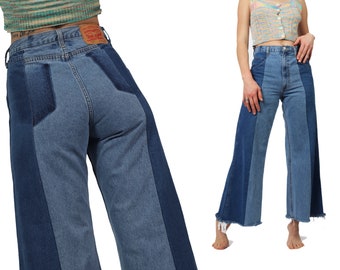 May include: A pair of blue denim jeans with contrasting panels of denim in a darker shade. The jeans have a wide leg and a frayed hem.