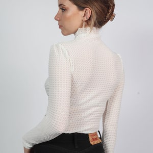 K&ouml;nnte beinhalten: Wei&szlig;es Langarmhemd mit Waffelstruktur und Stehkragen. Das Hemd ist kurz geschnitten und hat einen leicht bauschigen &Auml;rmel. Das Model tr&auml;gt eine schwarze Jeans.