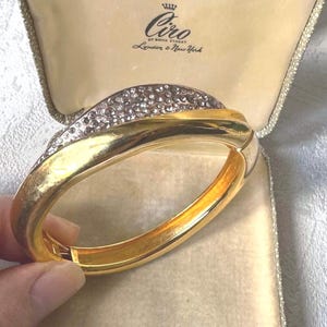 May include: A gold-plated hinged bracelet with a wave design, set with clear crystals. The bracelet is presented in a cream-coloured box, bearing the "Ciro of Bond Street London & New York" logo.
