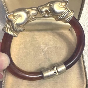 Peut inclure: Un bracelet vintage avec deux têtes de tigre dorées face à face. Le bracelet a un bracelet marron foncé, possiblement en écaille de tortue. Le fermoir est également doré. Le bracelet est présenté dans un écrin vintage.