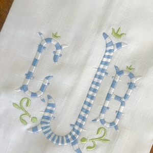 May include: A white linen tea towel with a blue and white striped embroidered monogram "CB" with green leaves and crowns.