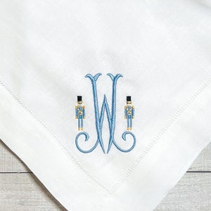 May include: White linen napkin with a blue embroidered monogram of the letter "W" with two blue toy soldier figures on either side of the letter.