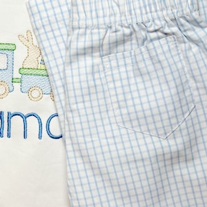 May include: A white and light blue gingham baby outfit with a white onesie and matching pants. The onesie has an embroidered design of a train with a bunny on top. The text "mama" is embroidered on the onesie.