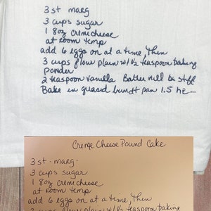May include: Handwritten recipe for a Creme Cheese Pound Cake on a white tea towel. The recipe calls for 3 sticks of margarine, 3 cups of sugar, 18 ounces of cream cheese, 6 eggs, 3 cups of flour, 1 1/2 teaspoons of baking powder, and 2 teaspoons of vanilla. The recipe instructs to bake the cake in a greased bundt pan for 1.5 hours.