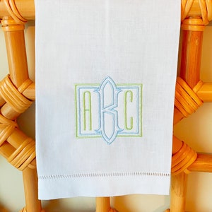 Pode incluir: Uma toalha de mão branca com um monograma bordado "ABC" em verde e azul em uma fonte decorativa.