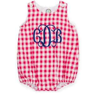 Pode incluir: Um macacão de bebê em xadrez rosa e branco com um monograma azul "COB" na frente.