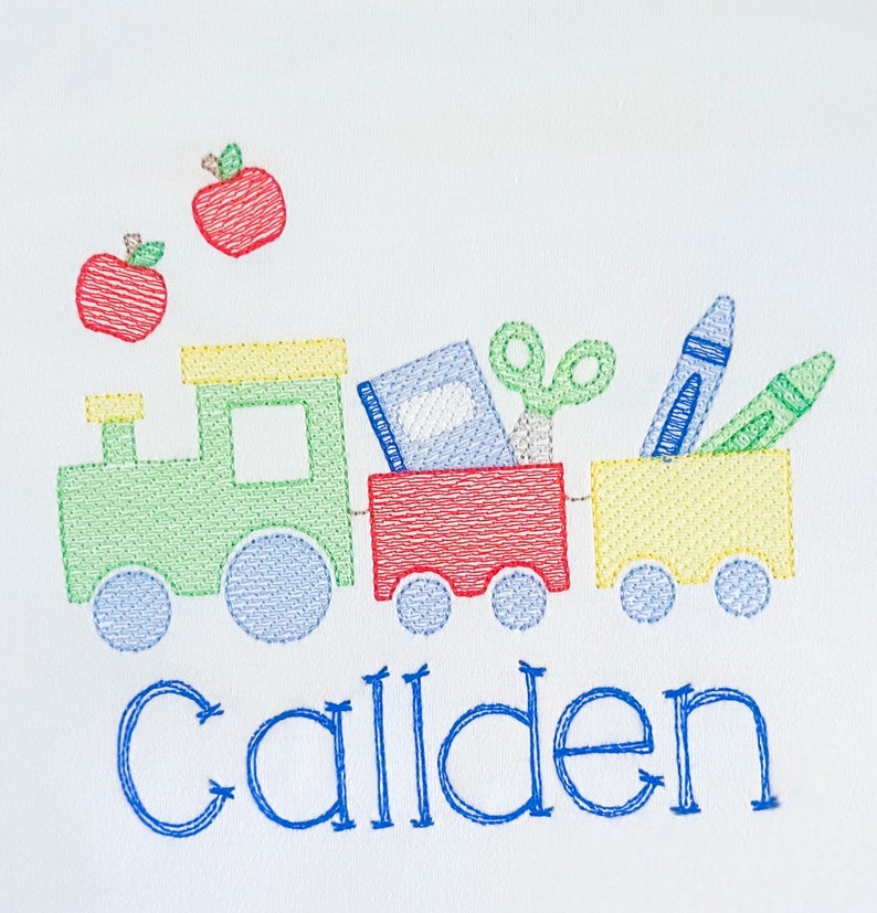 May include: Embroidered design of a green and yellow toy train carrying a red box, a blue book, a pair of scissors, a blue crayon, and a green crayon. Two red apples are above the train. The name "Callen" is embroidered in blue below the train.