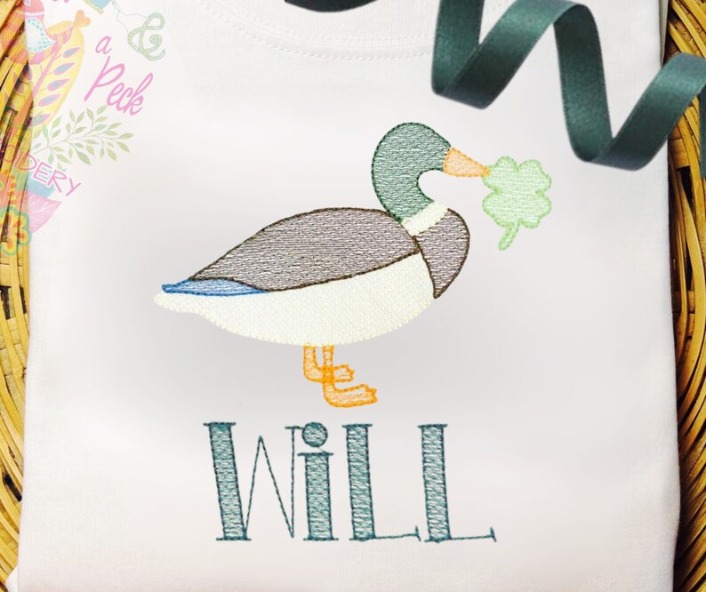 May include: Embroidered design of a green duck holding a shamrock in its beak, with the name "WILL" embroidered below.