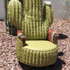 K&ouml;nnte beinhalten: Ein gr&uuml;ner Kaktus-f&ouml;rmiger Stuhl mit einer wei&szlig;en Bl&uuml;te oben. Der Stuhl hat einen braunen und roten gemusterten Stoff an den Armlehnen und ein gr&uuml;nes Kissen.