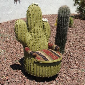 K&ouml;nnte beinhalten: Ein gr&uuml;ner Kaktus-f&ouml;rmiger Stuhl mit einem gemusterten Stoffbezug f&uuml;r Sitzfl&auml;che und R&uuml;ckenlehne. Der Stuhl steht auf einem Bett aus rotem Kies.