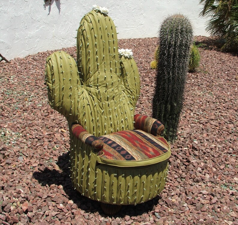 K&ouml;nnte beinhalten: Ein gr&uuml;ner Kaktus-f&ouml;rmiger Stuhl mit einem gemusterten Stoffbezug f&uuml;r Sitzfl&auml;che und R&uuml;ckenlehne. Der Stuhl steht auf einem Bett aus rotem Kies.