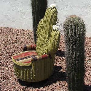 K&ouml;nnte beinhalten: Ein gr&uuml;ner Kaktus-f&ouml;rmiger Stuhl mit einem gemusterten Stoffkissen. Der Stuhl steht im Freien und ist von Kies umgeben.