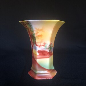 May include: A yellow, green, and red porcelain vase with a painted scene of a house and trees. The vase has a hexagonal shape and a flared opening.