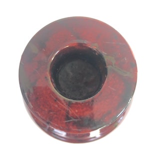 May include: A red and brown marble candle holder with a round top and a circular opening for a candle. The holder has a smooth, polished finish.