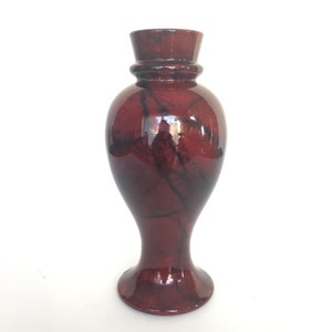 May include: A red and black ceramic vase with a marbled design. The vase has a wide base and a narrow neck.
