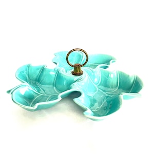 May include: A turquoise ceramic leaf-shaped serving dish with a gold-coloured handle. The dish has three sections and is designed to resemble a leaf. The handle is attached to the centre of the dish.
