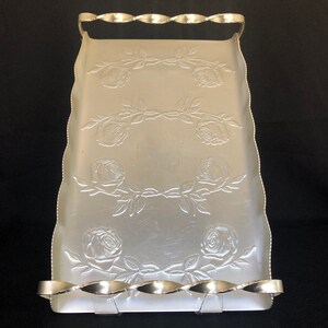May include: Silver serving tray with a decorative embossed rose pattern and a twisted wire handle.
