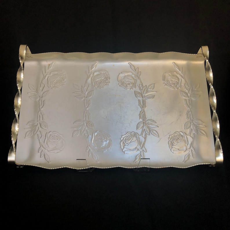 May include: A silver serving tray with a decorative rose pattern. The tray has a wavy edge and twisted handles.