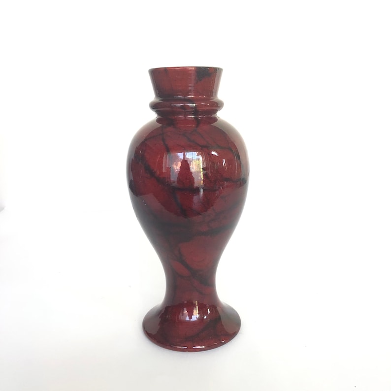 May include: A red and black marbled ceramic vase with a flared base and a narrow neck.