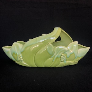 Könnte beinhalten: Ein grüner Keramik-Pflanztopf in Form einer stilisierten Blume mit einem Griff. Der Topf hat eine glänzende Oberfläche und eine hellgrüne Glasur.