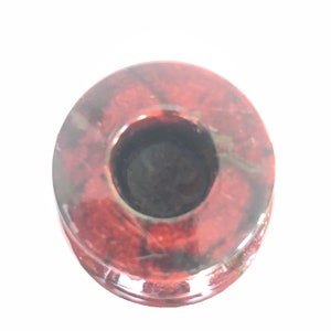 May include: A red and black stone candle holder with a round base and a circular opening for a candle.