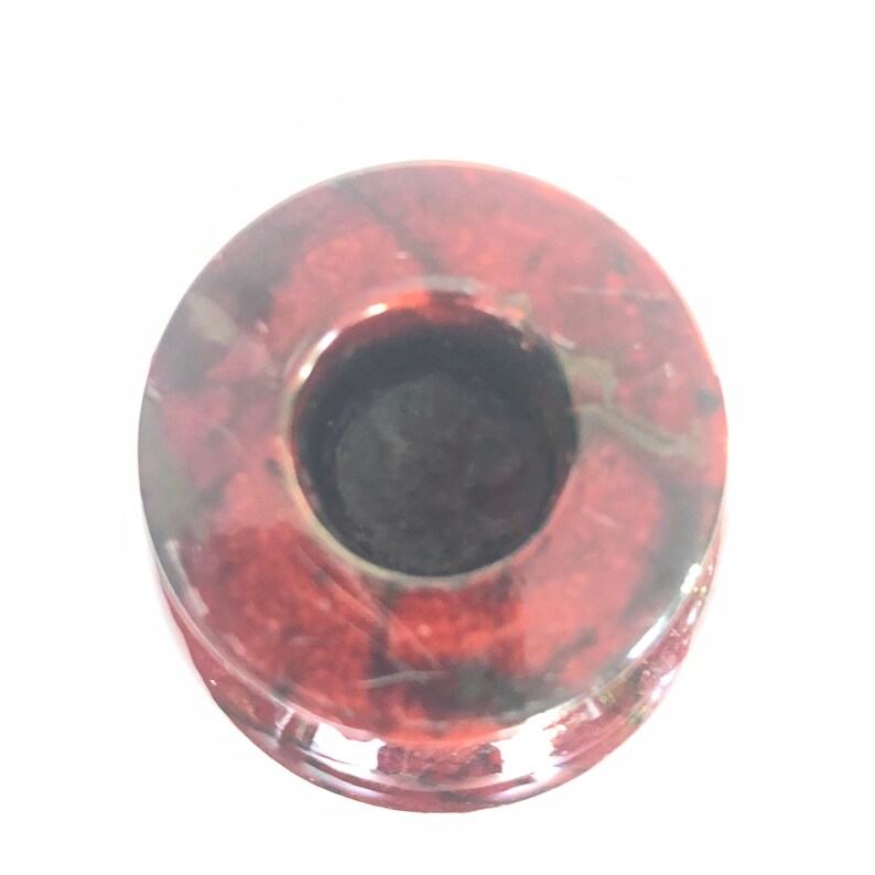 May include: A red and black stone candle holder with a round base and a circular opening for a candle.