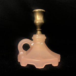 May include: A pink glass candle holder with a brass candle cup and a handle. The base of the holder has a scalloped edge.