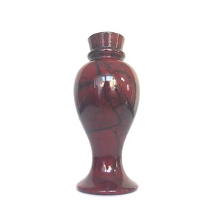 May include: A dark red ceramic vase with a marbled pattern. The vase has a wide base and a narrow neck.