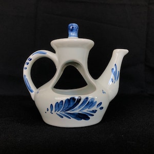 Może przedstawiać: Biały ceramiczny czajnik z niebiesko-białym wzorem Delftware. Czajnik ma dzióbek i uchwyt oraz otwór z boku.