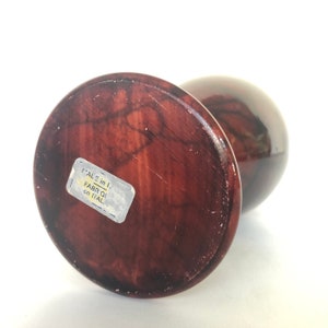 May include: A dark brown, round, wooden vase with a marbled pattern. The vase has a sticker on the bottom that reads "'ALE in I FABRIQ in ITAL".