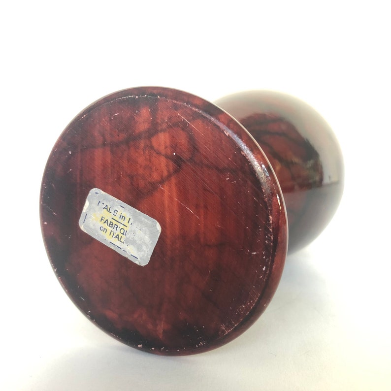 May include: A dark brown, round, wooden vase with a marbled pattern. The vase has a sticker on the bottom that reads "'ALE in I FABRIQ in ITAL".