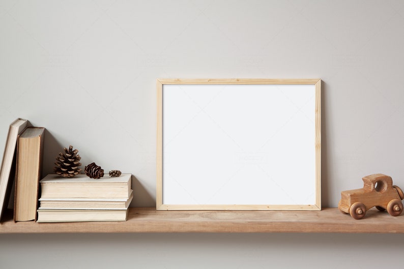 May include: A wooden shelf with a framed picture, a stack of books, pine cones, and a wooden toy truck. The shelf is against a light grey wall.