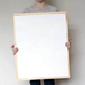 May include: A person holding a blank white framed poster in front of their body.