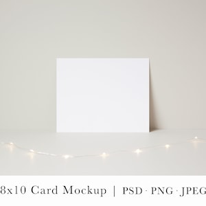 May include: A white 8x10 card mockup on a white surface with a string of white fairy lights in front of it.