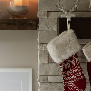 May include: A red and white Christmas stocking with a faux fur cuff hangs from a white antler hook on a stone fireplace.
