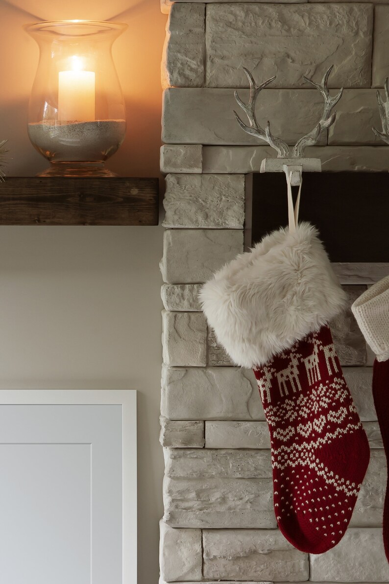 May include: A red and white Christmas stocking with a faux fur cuff hangs from a white antler hook on a stone fireplace.