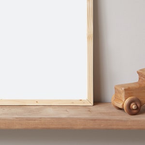 May include: A wooden toy car sits on a wooden shelf in front of a blank picture frame. The car is made of natural wood and has a simple design.