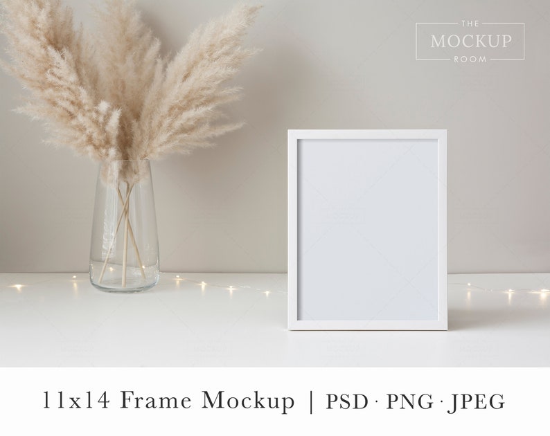 May include: White frame mockup with a white mat, sitting on a white surface with a vase of dried pampas grass and a string of fairy lights. The frame is 11x14 inches.