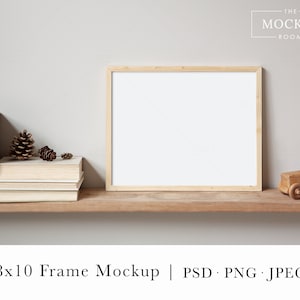 May include: A wooden shelf with a light wood frame mockup, a stack of books, pine cones, and a wooden toy truck. The text "THE MOCKUP ROOM" is in the top right corner of the image.