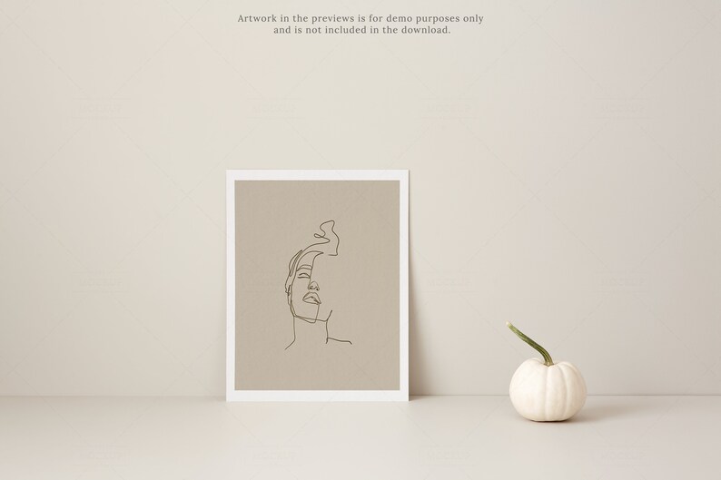 May include: A framed art print featuring a minimalist line drawing of a face, set against a neutral background. A small white pumpkin with a green stem sits nearby. The text "Artwork in the previews is for demo purposes only and is not included in the download." is visible.